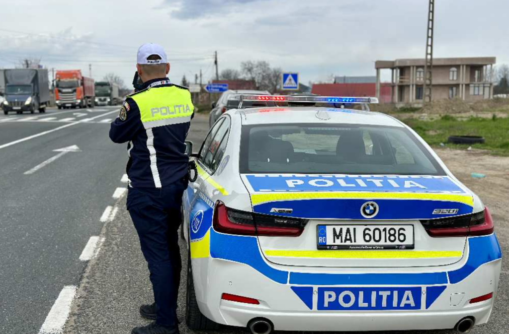 Un politist sta cu pistolul radar langa masina de Politie